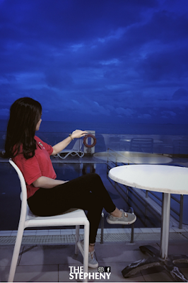 A girl in red shirt and black pant sitting on a white chair looking at the stunning seaview of penang 