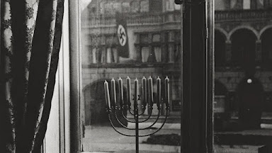 black and white image looking at a menorah, facing out a window at a Nazi building