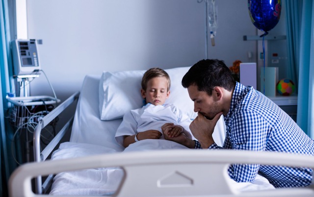 Male caretaker holding child's hand in a hospital bed