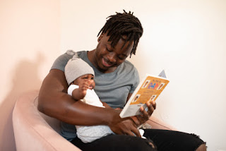 Picture of seated Black man holding his child, and holding a children's book. Photo from nappy.co