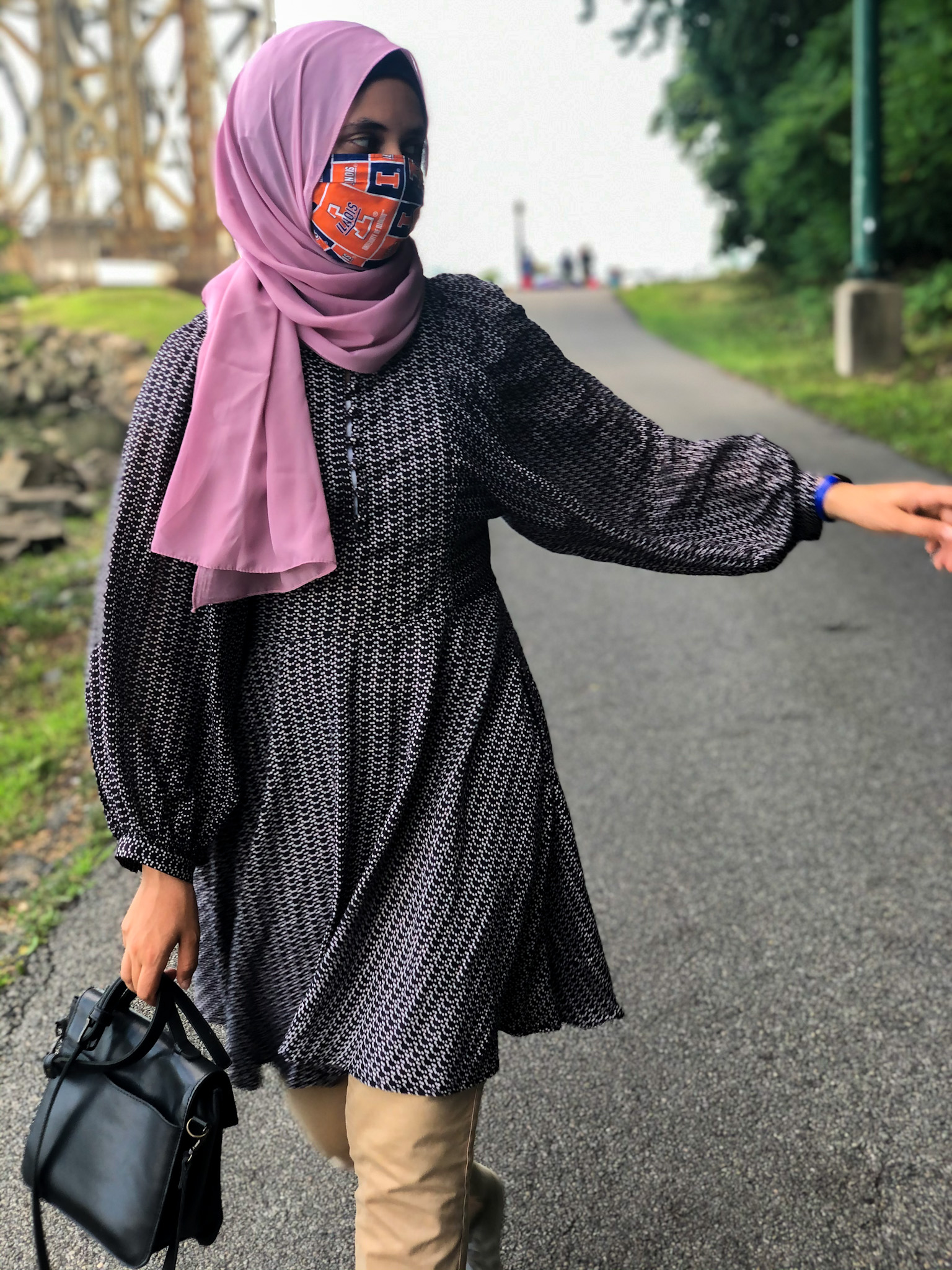 Sahara walking, black bag in right hand, pink scarf, pointing with left hand to the left