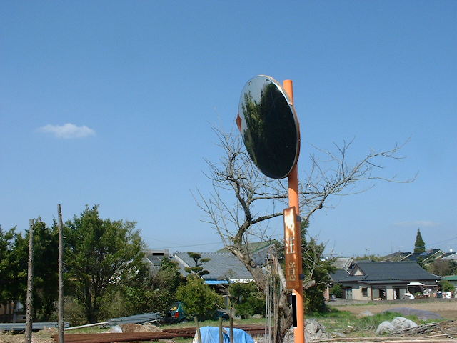 A photo of a rural town in Japan with a blue sky in the background and a round traffic mirror in the foreground.