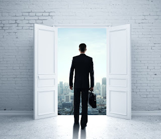 A man with a briefcase is walking out open doors that look out over the city