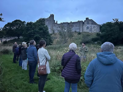 A line of people stand in a wildflower meadow in front of Haddon Hall.