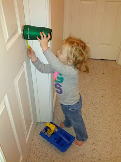 Lily holding a cup over the doorknob and using a plastic screwdriver