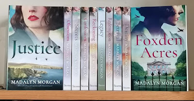 Bookshelf containing the Sisters of Wartime England series by Madalyn Morgan. The novels Justice and Foxden Acres are facing outwards with their covers displayed. Spines of the remaining titles are visible.