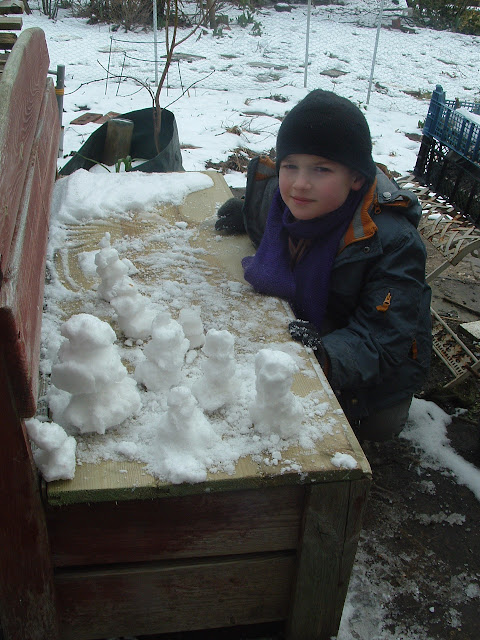 A little boy posing with a posse of tiny snowmen on a garden bench