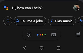 A screenshot of the screen that pops up when the circle symbol in the previous image is pressed for a second or two. The sentence "Hi, how can I help?" appears at the top, with some options below it labelled "Play music" and Turn up volume". Underneath that are three more symbols: the one on the left looks like a filled circle inside a square with rounded corners, one of which is missing and replaced with a small dot. The one in the middle is made up of four dots in a line, coloured blue, red, yellow, and green respectively. The one on the right is a small icon of a computer keyboard.