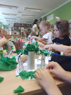 Dzieci siedzą przy stoliku i wykonują prace plastyczne drzewo jawor z rolki po papierze toaletowym i bibuły.