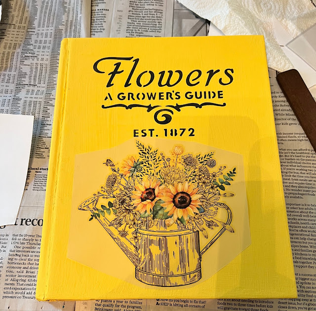 Photo of an old book painted yellow with botanical stencil and decor transfer.