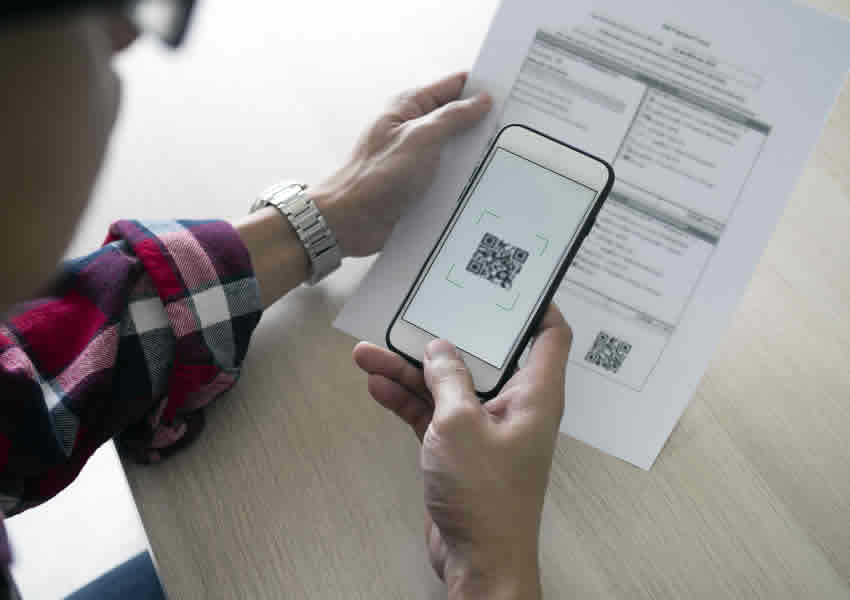 Imagem mostra uma pessoa apontando seu Smartphone para um boleto onde está sendo feito o pagamento via QR Code do pix.