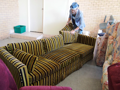 A man arranging the back cushions of a green, fawn and black striped sofa in a warehouse.