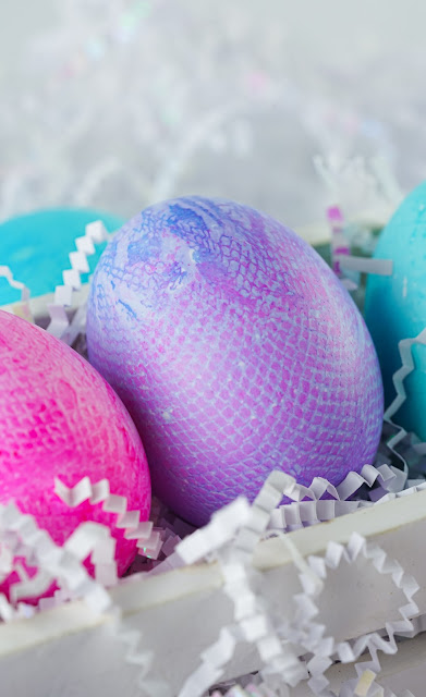 dyed eggs in a white box with white crinkle paper shreds.