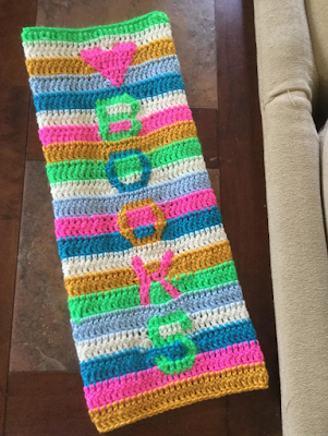 Narrow swatch of striped crochet fabric, with a heart symbol and letters spelling 'BOOKS' arranged vertically along it