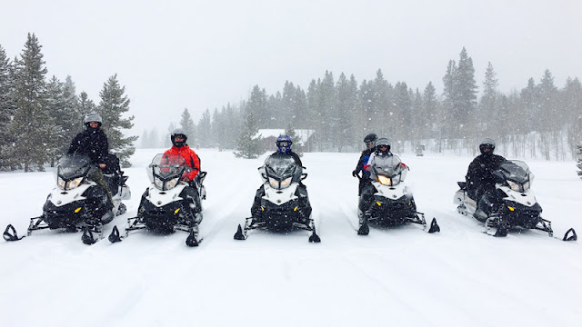 five snowmobile riders lined up as snow falls