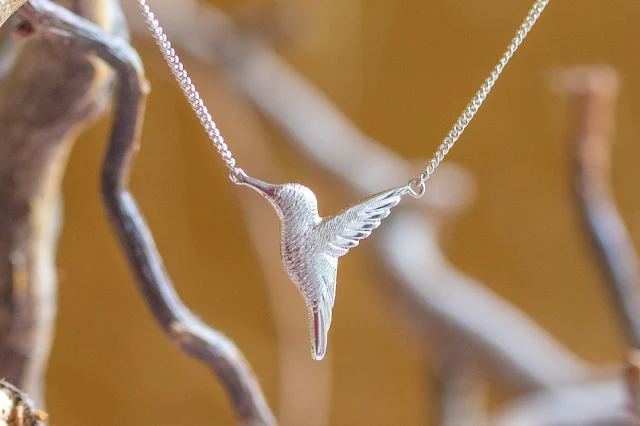 Silver hummingbird necklace against gold background and twigs