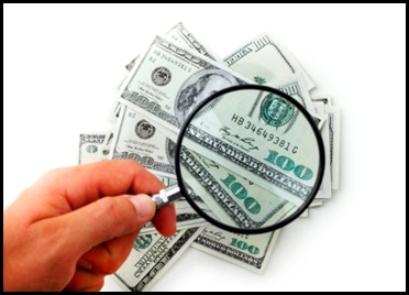 Human hand holding a magnifying glass over a bunch of currency notes