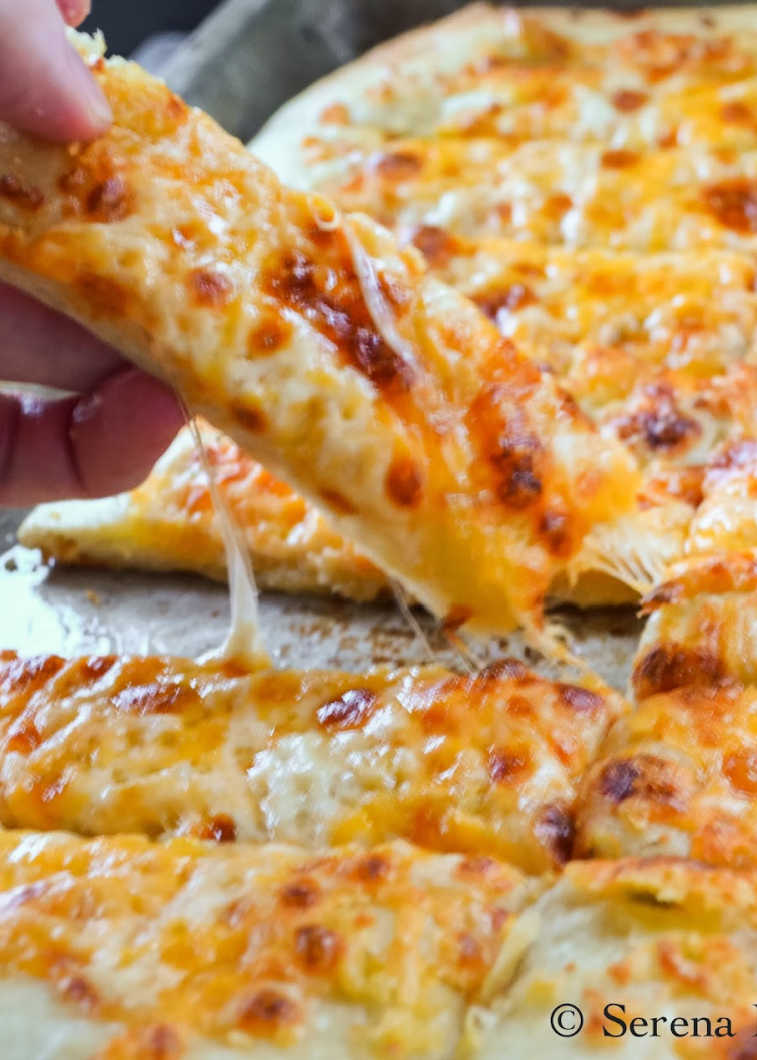 A hand pulling a Cheesy Breadstick away from the rest of the Pizzeria Style Cheesy Breadsticks in a pan.