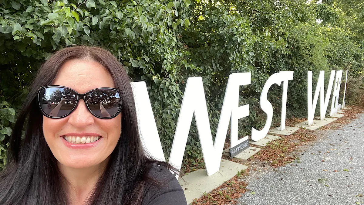 A lady with dark sunglasses smiles into the camera with the Westwell Wines letters in the background | Westwell Wines, Kent