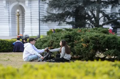 Dos personas disfrutando de una sesión de fotografía al aire libre en un evento cultural en La Plata, con asistentes y arquitectura clásica de fondo