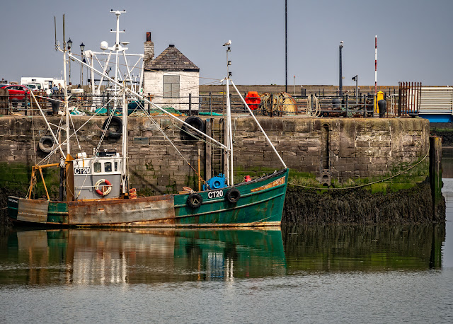 Photo of a fishing boat reflected in the still water in Maryport Harbour