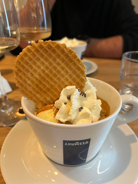 A coffee cup with coffee, ice cream and cream and a circular wafer