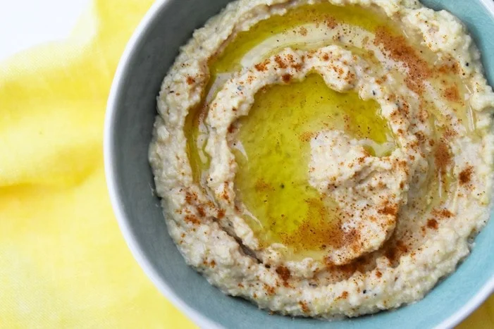 close up on homemade hummus in blue bowl on yellow napkin