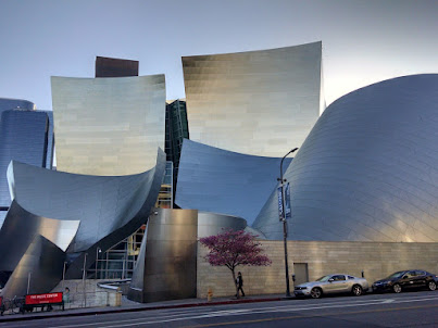 Photo of a building whose exterior is constructed of many small sheets of shiny silver metal connected to make huge irregular planes at different angles.