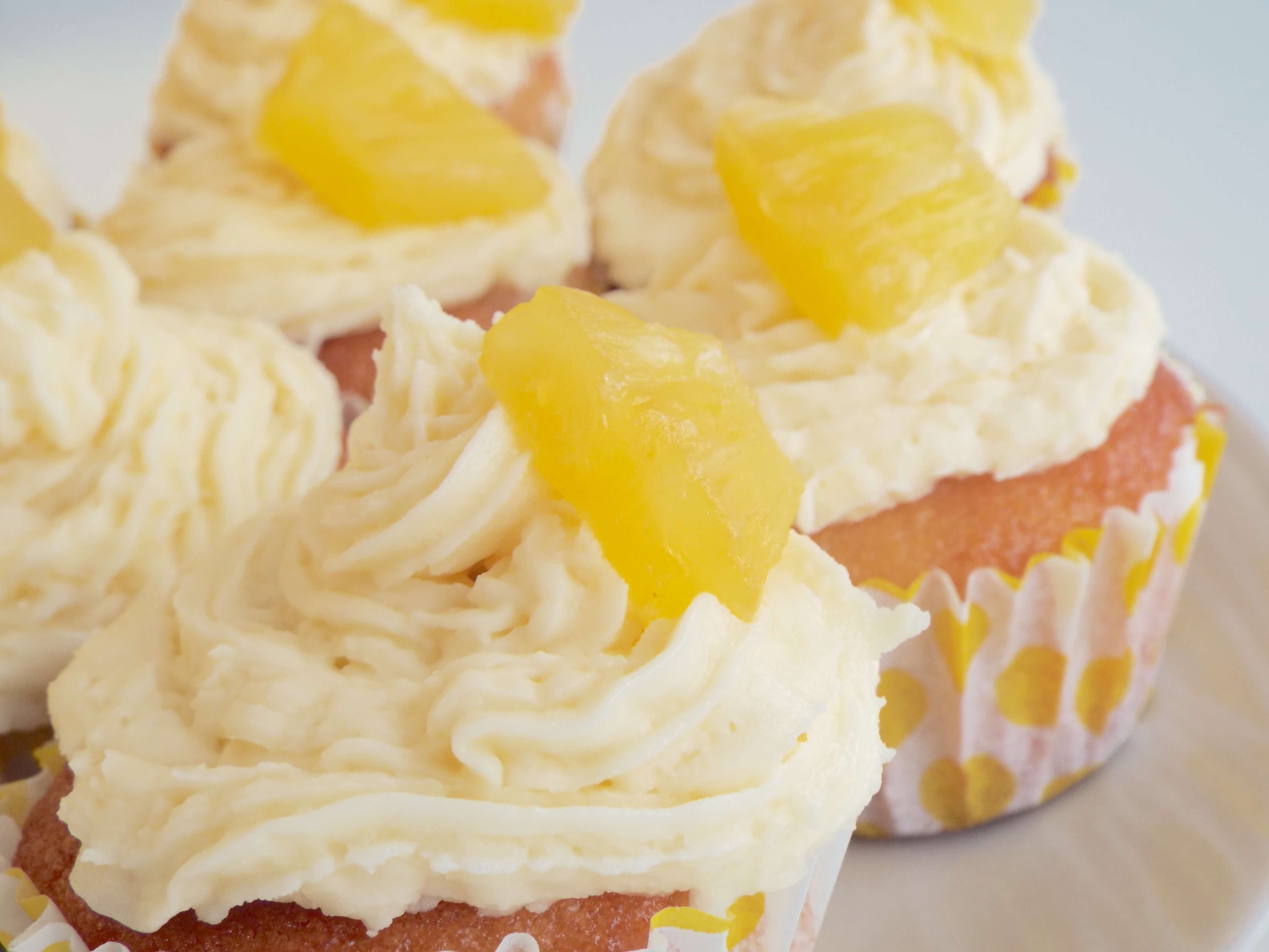 Close up shot of swirled buttercream icing and sugared pineapple on top of cupcake, amongst other buttercream swirl iced cupcakes.