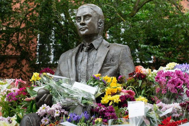 Statue of Alan Turing holding an apple and surrounded by flowers