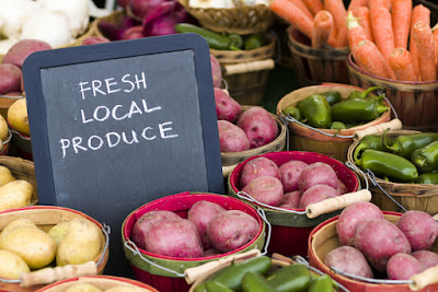 A photo of several different kinds of vegetables sorted into separate buckets. There is a sign that reads, "Fresh, local, produce."