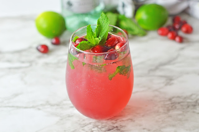 mojito in a clear glass with cranberry and mint garnish.