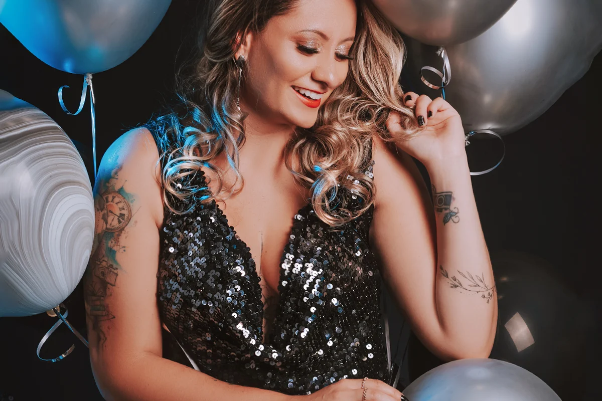 woman surrounded by balloons in a sequined party dress poses for the camera