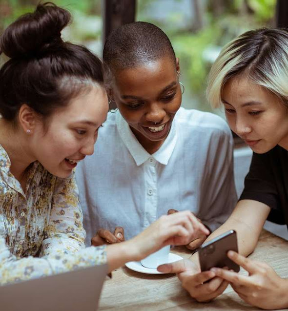Three smiling young women looking at a cell phone.