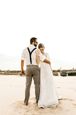 Novio abrazando a la novia, ella con la cabeza en su hombro, ambos en una playa