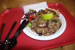 A heaping mound of brown fried rice with pieces of white egg with strips of white Chicken meat with a wedge of bright green lime on a red tray on a bright background. 