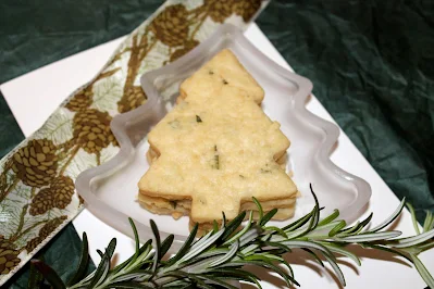 Baked rosemary shortbread Christmas tree shaped cookies on a small Christmas tree shaped dish with a rosemary garnish.