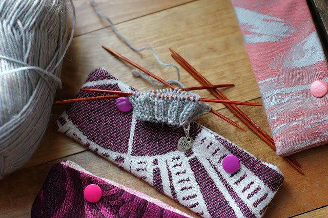 Heathered grey sock cuff in the works on double pointed needles with holders next to it.