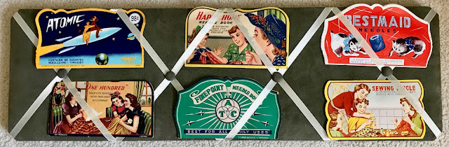 6 vintage needle packages with colorful fronts on a display board.