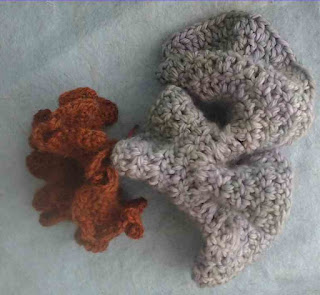 Two crochet coral models, one is smaller and made with brown yarn, the other is larger, and made with green bulky yarn.