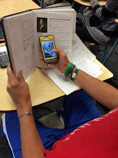 A student looks at a cell phone hidden behind a text book.