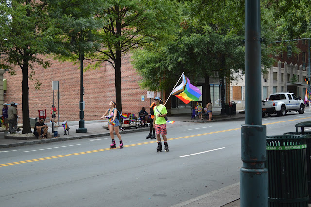 People skating down the middle of the road with pride flags.