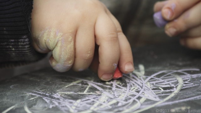 Mani di bimbo che disegna con i gessetti colorati