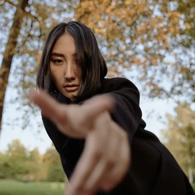 A young woman dressed in black pointing threateningly at the camera.
