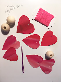 Holzperlen und rote Herzen aus Papier werden zu einer Girlande
