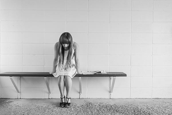 Una mujer sentada en un banco mira reflexiva al suelo.