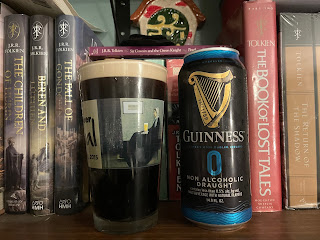 A pint glass filled with Guinness 0.0 beside the beer's empty can.