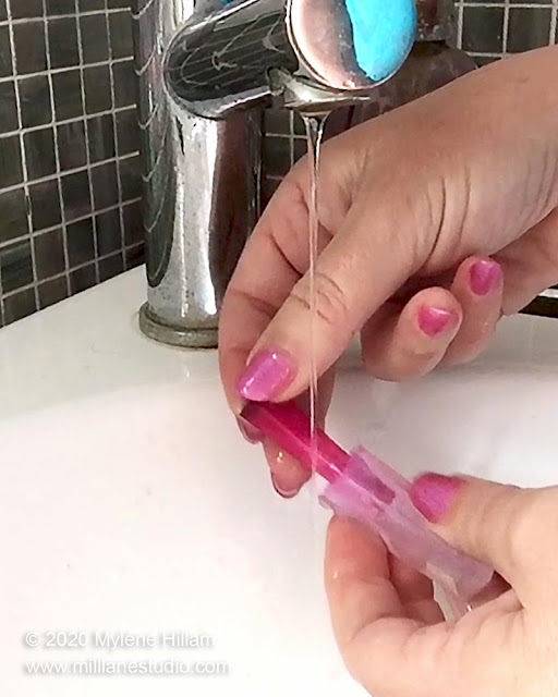 Hand under running water removing slender resin crystal from a silicone mould