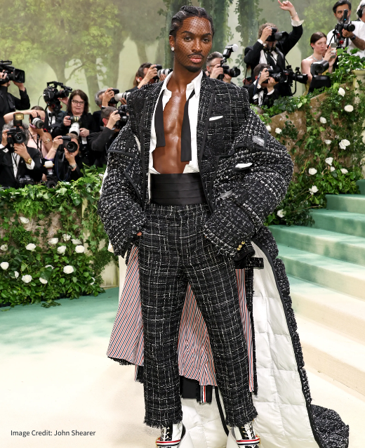 Photo of Alton Mason at the 2024 Met Gala. He is wearing Thom Browne - an oversized tailcoat with train, open shirt with undown bow tie, tweed trouers and oversized heeled boots.