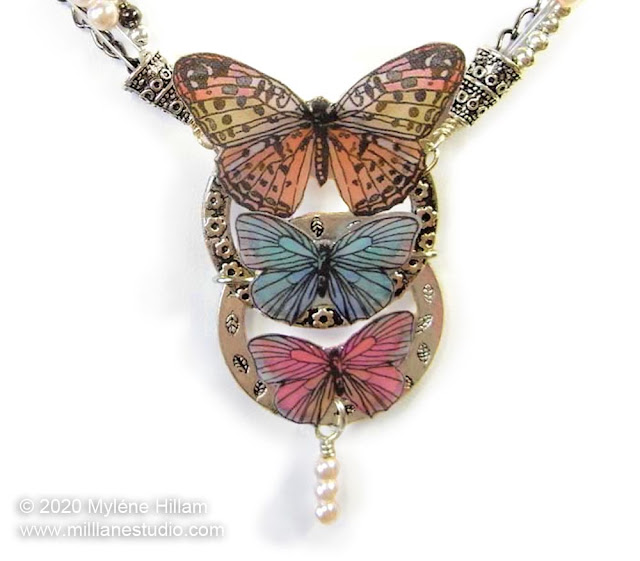Butterfly and pearl necklace with 3 pastel butterflies attached in descending sizes to 2 vertically connected metal rings.